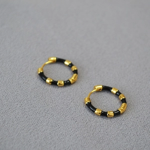 Macro shot of gold-plated bamboo-style earrings with black enamel sections on fabric