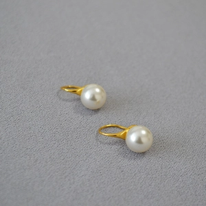Élégantes boucles d'oreilles crochet en or avec perles rondes blanches sur tissu gris