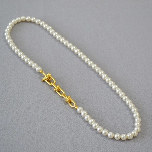 Détail de perles blanches élégantes et fermoir à maillons en U dorés sur un collier