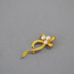 Macro shot of gold bow brooch with textured metallic ribbons and three white pearls