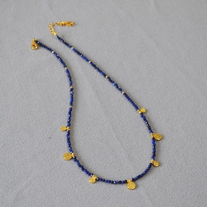 Détail macro du collier de perles bleues avec un pendentif pièce dorée gravée