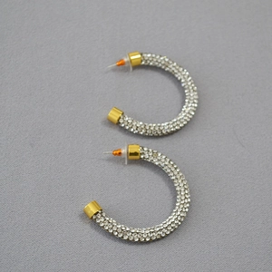 Macro detail of gold-plated C-shaped hoop earrings with sparkling white crystals