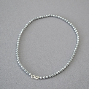 Detailed close-up of grey pearl necklace featuring a silver infinity clasp on fabric