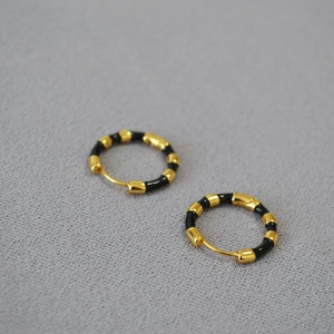 Detailed view of bamboo-shaped gold earrings with black enamel on a textured surface