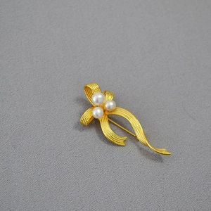 Macro shot of gold ribbon brooch with freshwater pearls and fine brushed metal texture
