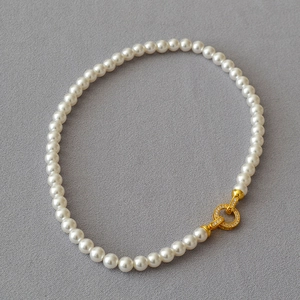 Elegant pearl necklace with gold zircon encrusted double-ring clasp on gray background