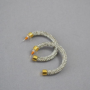 Detail of C-shaped gold-plated hoop earrings with dense white rhinestones on grey fabric