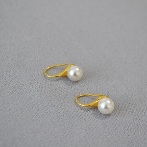 Boucles d'oreilles crochet dorées avec perles blanches brillantes sur fond en tissu gris