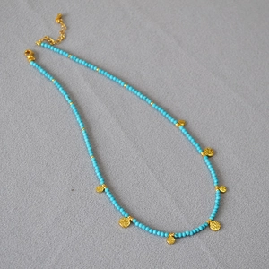 Détail du collier de perles turquoise avec breloques pièces dorées et fermoir