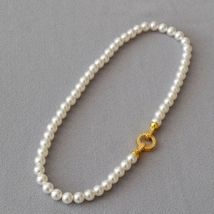Macro shot of 8mm round white pearl necklace with gold crystal-studded circular clasp