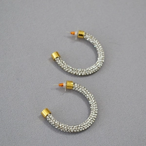 Detail of C-shaped gold plated brass earrings with pave set sparkling white rhinestones