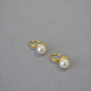 Détail de boucles d'oreilles perles blanches avec crochets dorés sur tissu gris