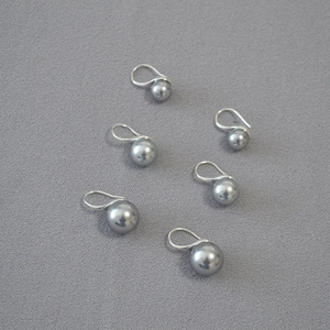 Set of 6 minimalist grey pearl earrings with silver hooks on dark fabric background
