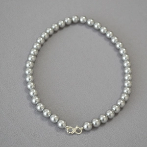 Detail of grey pearl necklace with silver infinity clasp on textured fabric