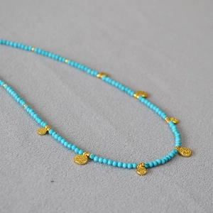 Vue détaillée du collier en perles turquoise avec des breloques dorées en forme de pièces