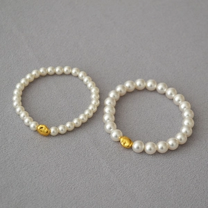 Detail view of two white pearl bracelets featuring unique irregular gold beads on grey fabric
