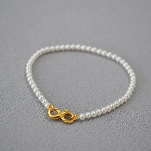 Detail of high-gloss round pearl necklace with gold lobster clasp on grey background