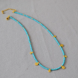 Collier en perles de turquoise avec pendentifs pièces dorées sur fond gris texturé