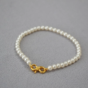 Macro detail of high-luster white pearls with a golden S-shaped infinity clasp on gray fabric
