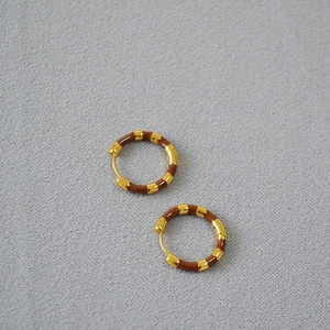 Close-up of gold-plated brass hoop earrings featuring rich brown enamel inlay segments