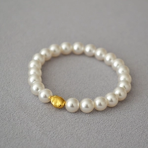 Baroque pearl bracelet with central gold bead on grey textured fabric background