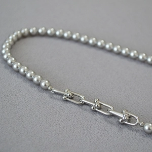 Détail macro des maillons en U et des perles grises sur un collier de mode de luxe
