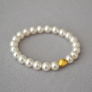 Macro detail of white high-gloss pearls with an irregular gold accent bead on elastic band