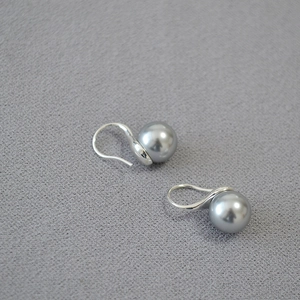 Detailed view of silver hook earrings featuring high-luster grey pearls on grey fabric