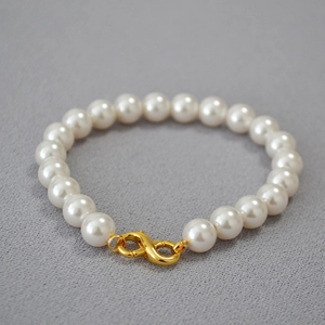 Close-up of elegant round pearls with a golden infinity clasp on a soft fabric background