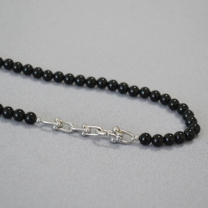 Macro detail of U-shaped metal link clasp on a black beaded chain necklace