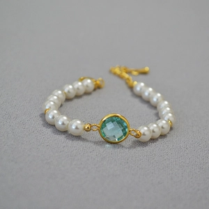 Detail of white pearl bracelet featuring a faceted light blue crystal and gold-plated chain