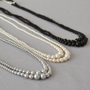 Three-layer gradient faux pearl necklaces in grey, white, and black on fabric