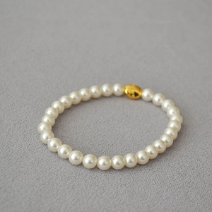 Detailed view of elastic pearl bracelet with baroque golden bean on gray background