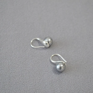 Flat lay of gray round pearl earrings on a textured surface with silver hooks