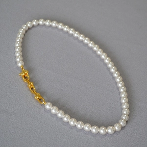 Détail d'un collier de perles élégant avec fermoir à maillon en U doré sur fond gris