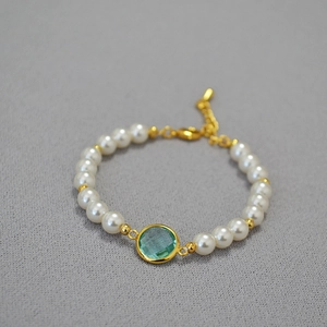 Detail view of pearl bracelet featuring faceted green gemstone and gold-plated hardware