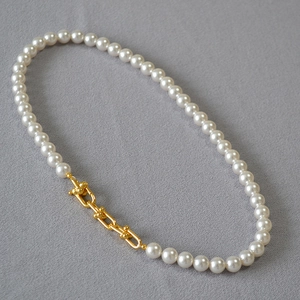 Détail d'un collier de perles élégant avec maillons métalliques en U dorés sur tissu gris