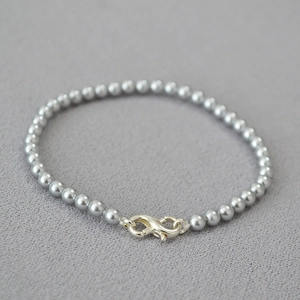 Detail of grey pearl bracelet featuring a silver infinity clasp on textured fabric