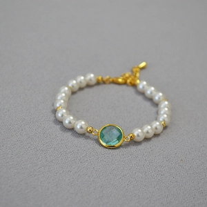 Detail of white round pearls bracelet with a green faceted gemstone and gold lobster clasp