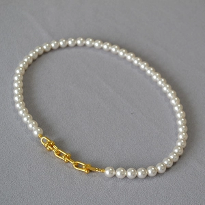 Détail de perles blanches reliées par des boucles de chaîne en U dorées sur tissu gris