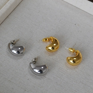 Detail view of water drop earrings in polished gold and silver finish on linen