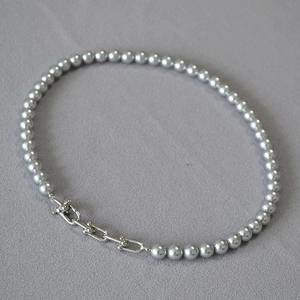Détail d'un collier de perles grises avec trois maillons en U en métal industriel