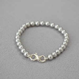 Detail of gray pearl bracelet featuring a silver infinity clasp on textured fabric