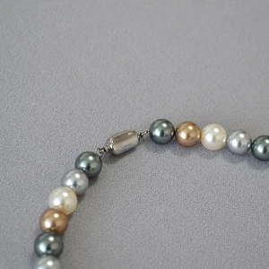 Macro shot of multi-color pearl necklace with silver oval clasp detail on grey background