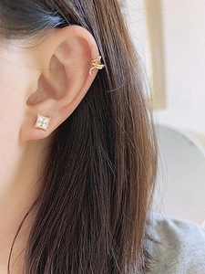 Detailed view of gold snake ear cuff and white shell floral stud earring on model ear