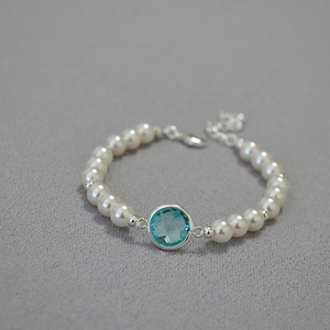 Macro detail of round white pearls with a faceted blue crystal and silver lobster clasp