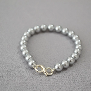 Detail of grey imitation pearl necklace featuring a silver infinity clasp on textured fabric