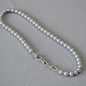 Détail du collier de perles grises avec fermoir en U argenté sur tissu texturé gris