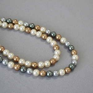 Detail of vintage round pearls in champagne, gray and green tones on dark fabric