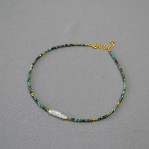 Macro detail of turquoise beaded necklace featuring a white baroque pearl and gold clasp